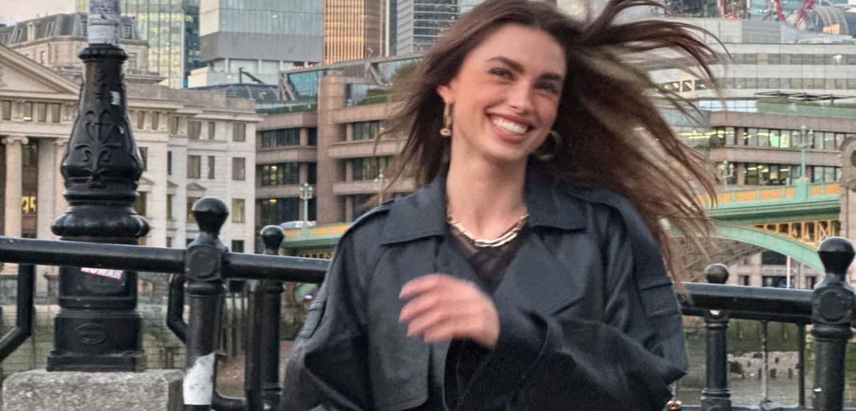 Veste en cuir noir avec une coupe décontractée, superposée sur un haut sombre, placée devant un paysage urbain avec des gratte-ciels et un pont.