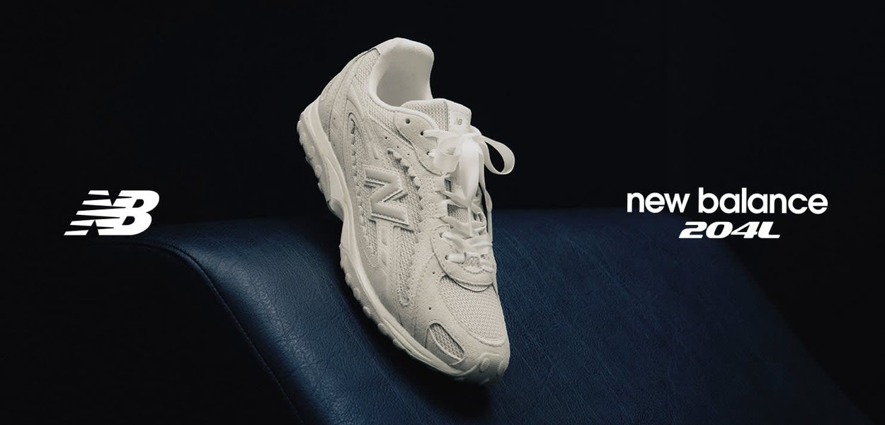 Zapatilla New Balance 204L blanca apoyada sobre una superficie oscura texturizada con un fondo negro que presenta el logotipo y texto de New Balance.