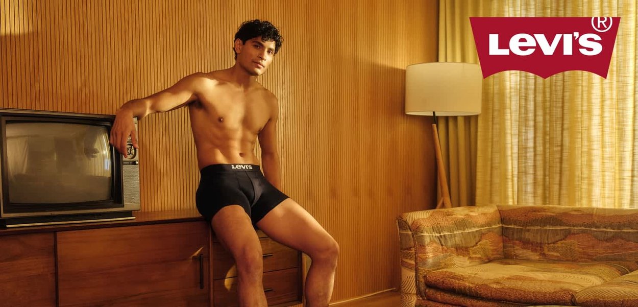 Levi's schwarze Baumwoll-Boxershorts für Herren mit Logo-Taillenbund. Hintergrund aus Holzpaneelen, Retro-Fernseher und gemusterte, strukturierte Couch.