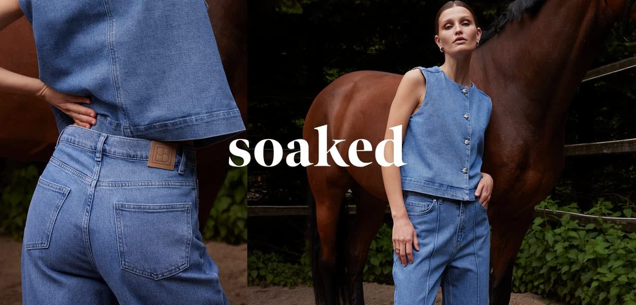 Frau trägt ärmelloses Denim-Oberteil und Jeans, steht neben einem braunen Pferd in einer grünen Außenanlage mit Holzzaun.