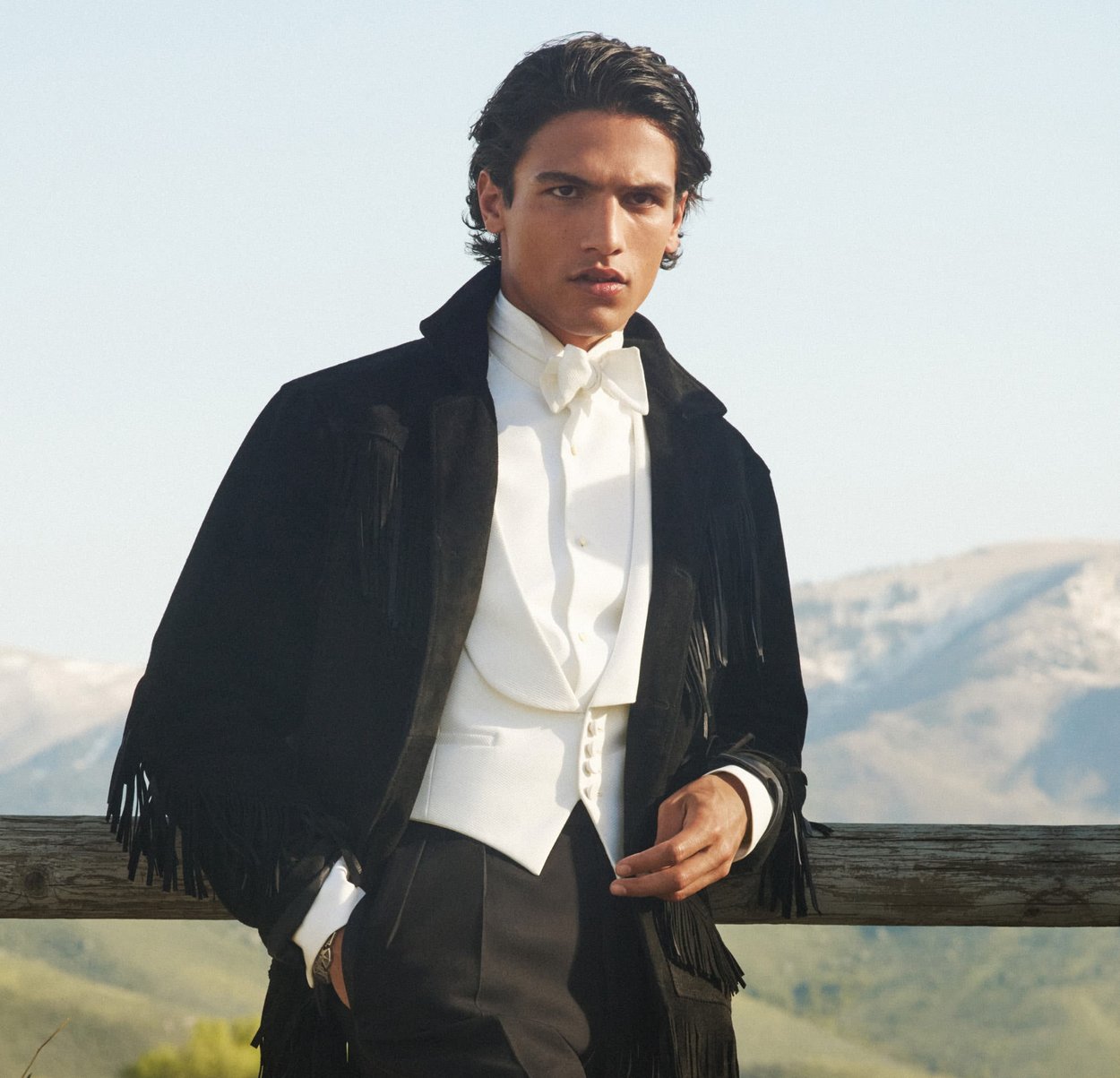 Svart mockajacka med fransdetaljer, vit väst och fluga. Modellen står mot en bergig bakgrund.