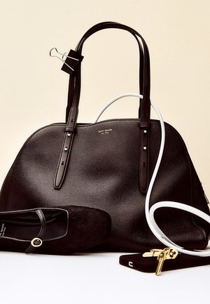 Schwarze Ledertasche mit glatter Textur und zwei Griffen. Dazu ein schwarzer flacher Schuh mit weichem Finish und ein Schlüsselanhänger.