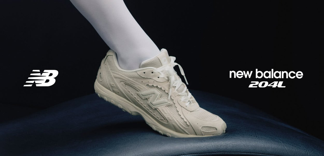 Pie con zapatilla beige New Balance 204L sobre una superficie oscura, con el logo de New Balance y el nombre del modelo en un fondo negro.