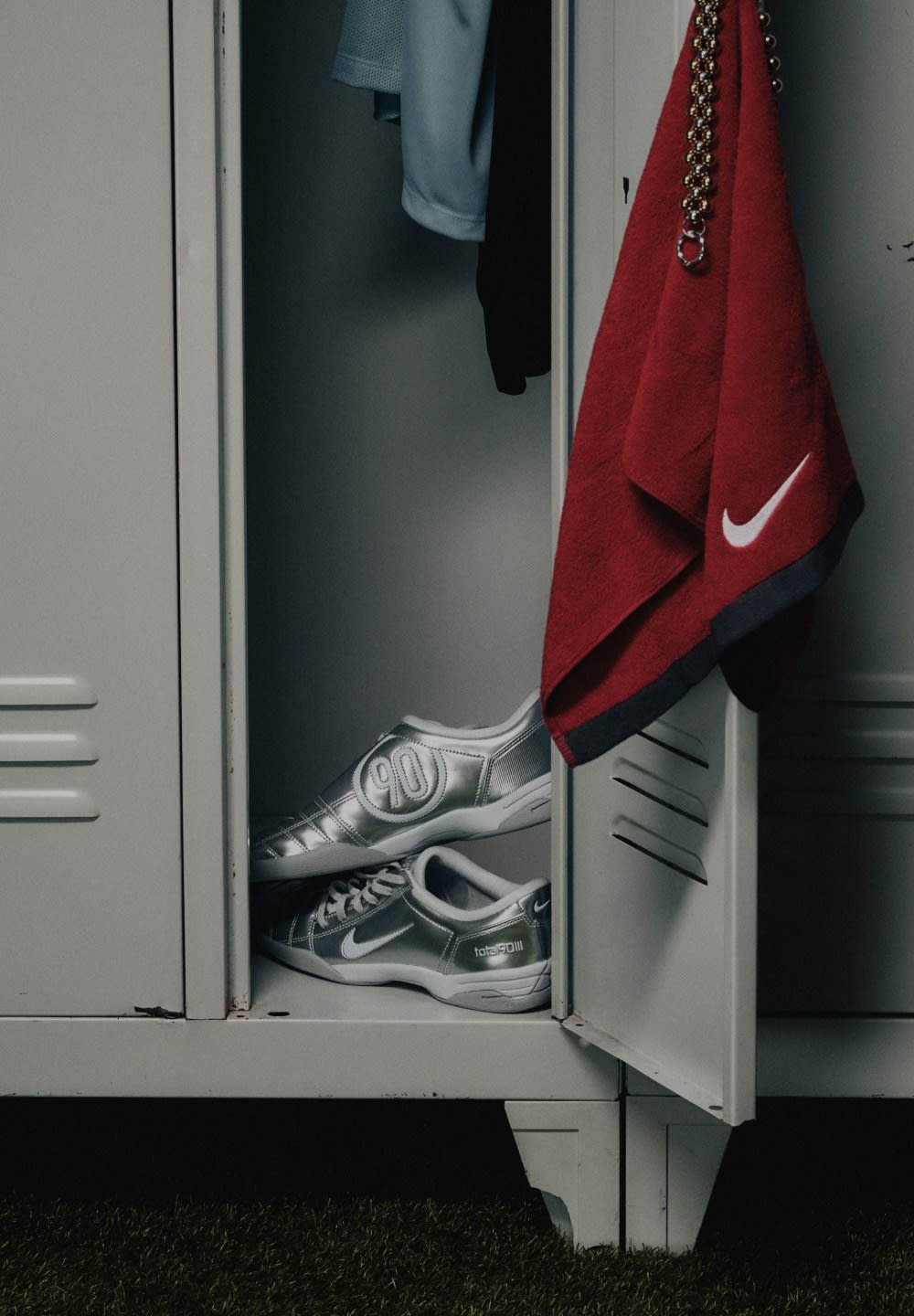 Silver athletic shoes with black laces and a large "90" printed on the side, placed inside an open locker next to a red towel.