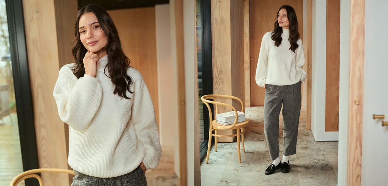 Vitt stickat sweater med ett strukturerat mönster, kombinerat med grå rutiga byxor. Modellen står i en modern inredning. Svarta skor och vita strumpor kompletterar looken.