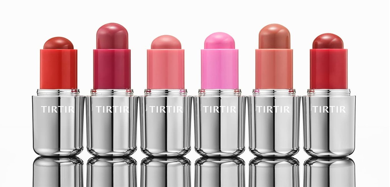Sei rossetti aperti in varie tonalità di rosso, rosa e marrone con custodie argentate, etichettati TIRTIR, disposti in fila su una superficie riflettente.