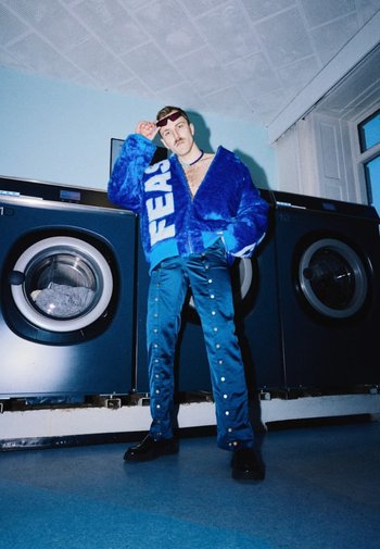 Blå pelskåbe med teksten "FEAR", parret med blå bukser med sølvnitter. Brugeren står i et vaskeri ved vasemaskinerne.