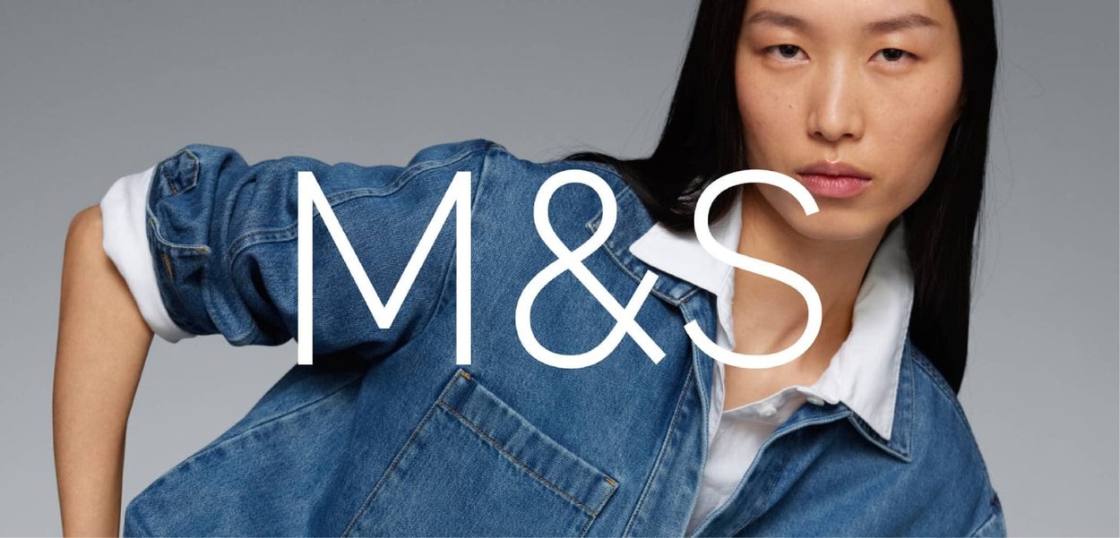 Veste en jean avec une coupe décontractée, couleur bleu clair, couture visible, et une chemise blanche à col en dessous. Texte en gras superposé : "M&S."