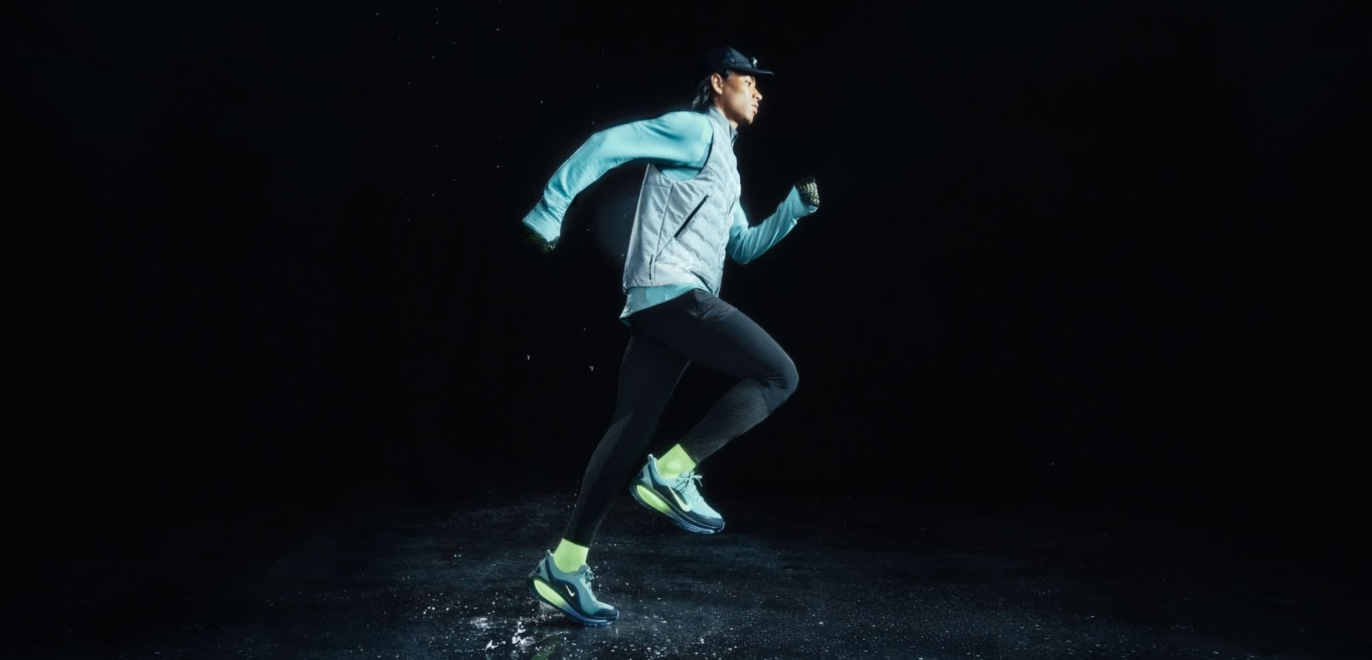 Athletic apparel featuring a light gray quilted vest, long black leggings, and blue running shoes with neon accents, set against a dark background.
