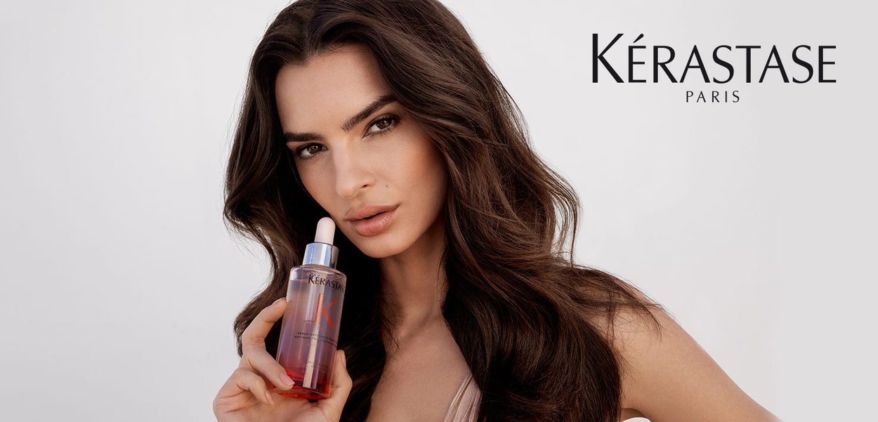 Olio per capelli Kérastase in una bottiglia trasparente, liquido rosa e dettagli argentati. Presenta un tappo con contagocce; l'etichetta include il nome del marchio.