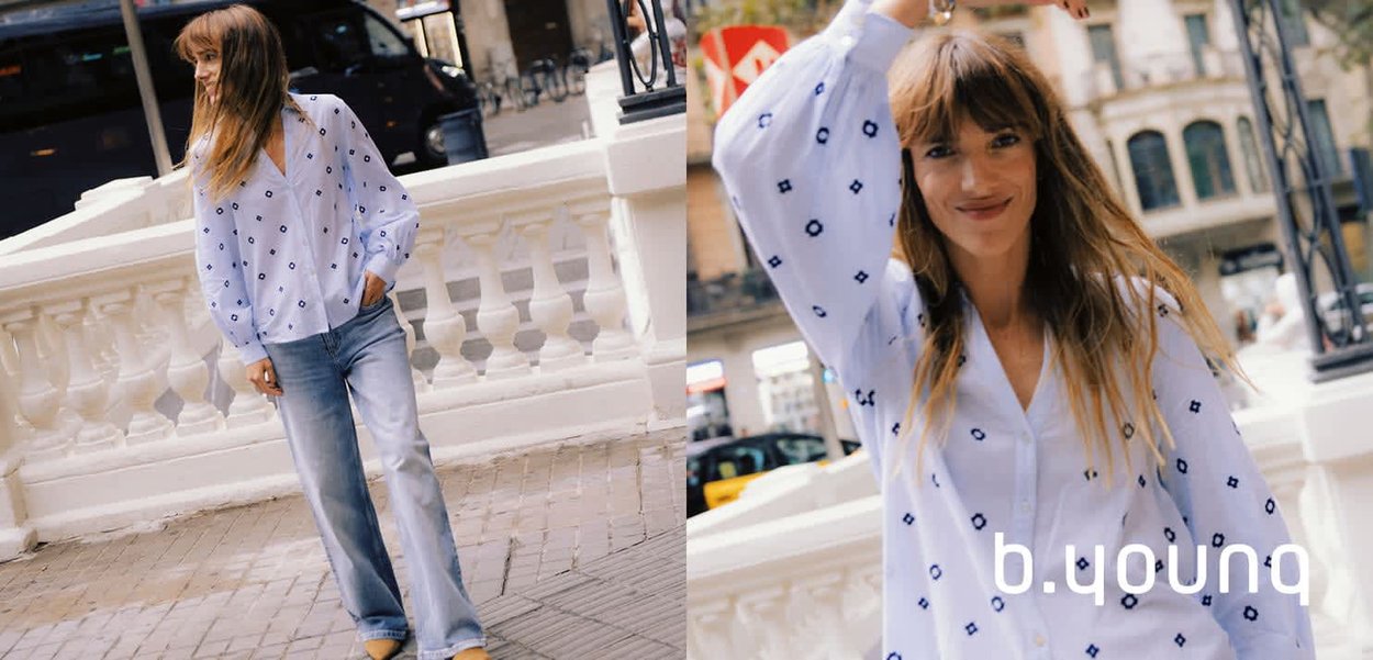 Frau mit langen braunen Haaren, die eine weiße Bluse mit blauen Rautenmuster und Schlagjeans trägt, posiert im Freien neben einem weißen Geländer.