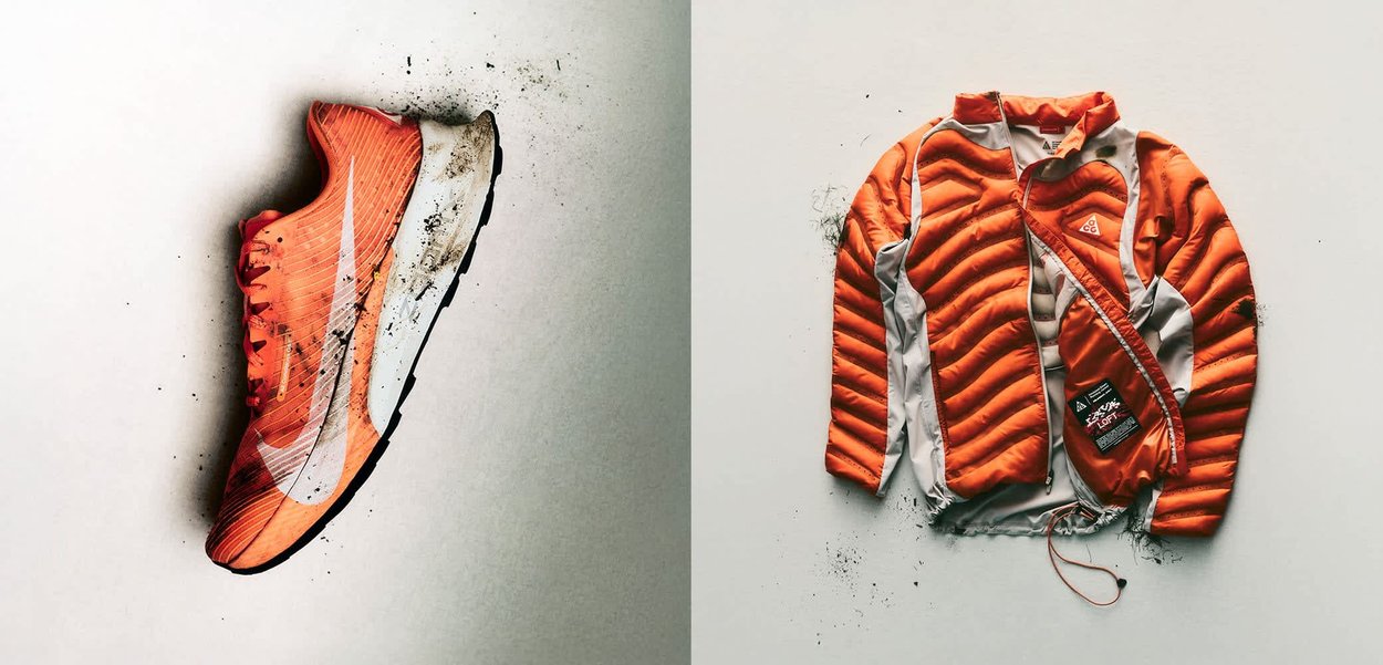 Chaqueta aislante naranja y gris con cremallera parcialmente abierta, mostrando la etiqueta interior, descansando sobre una superficie blanca con manchas de suciedad cerca.