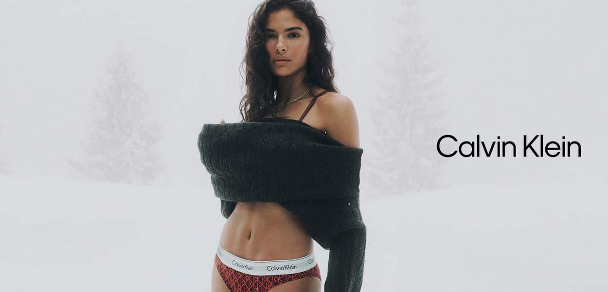 Ropa interior Calvin Klein en blanco, con una cintura roja estampada. El modelo lleva un suéter oscuro y oversize, ambientado en un paisaje nevado.