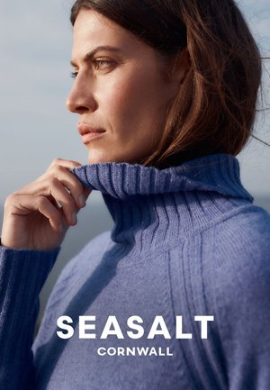 Blauer gerippter Rollkragenpullover aus weichem Material mit hohem Kragen und strukturiertem Strickmuster, vor natürlichem Hintergrund gezeigt.