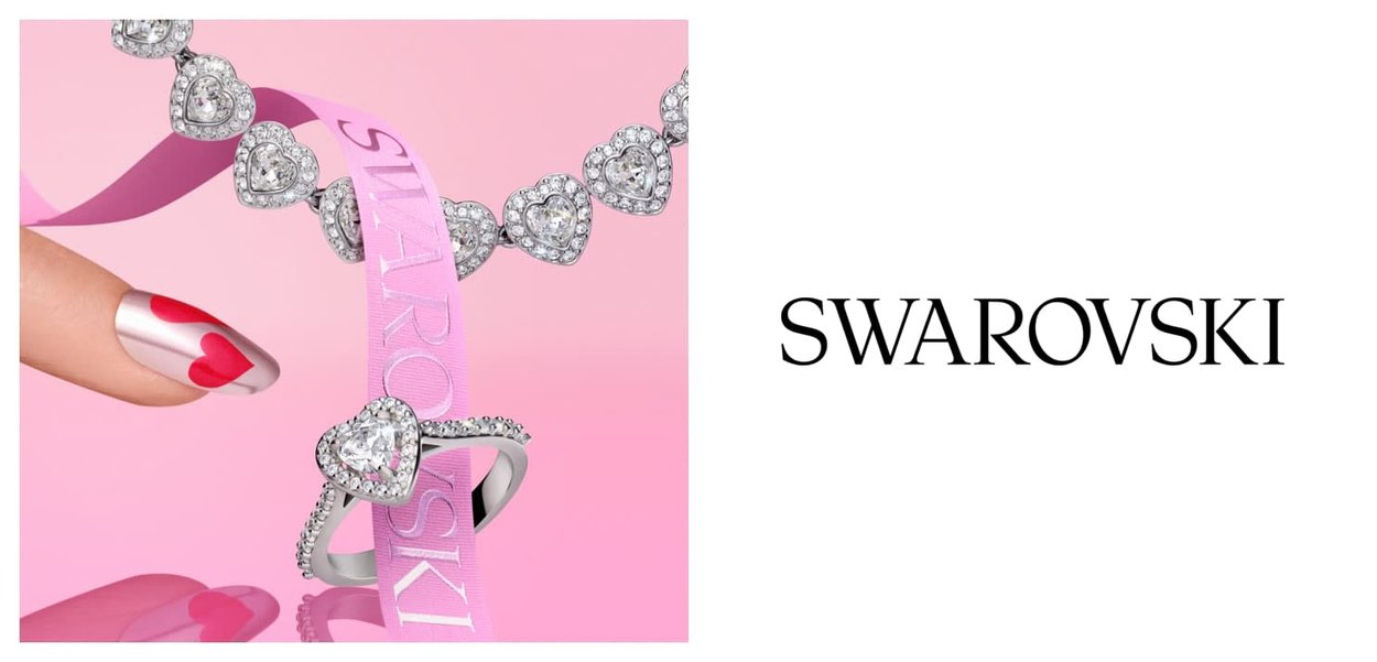 Dłoń z czerwono-srebrnym zdobieniem paznokci w kształcie serca obok pierścionka i bransoletki w kształcie serca z kryształu na różowym tle z wstążką "Swarovski".