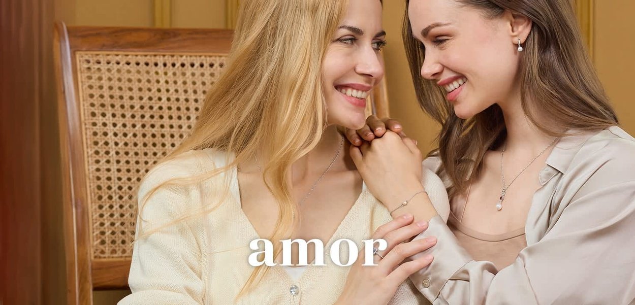 Due donne condividono un momento, indossando collane d'argento con ciondoli. Una ha delle perle naturali, mentre l'altra indossa un outfit a strati.