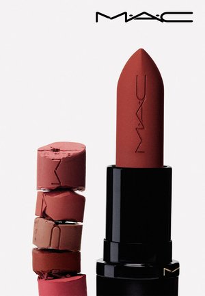 MAC-lipstick in matte rood met merknaam erin gegraveerd, naast gestapelde, gebroken stukjes lipstick in verschillende bruine en rode tinten.