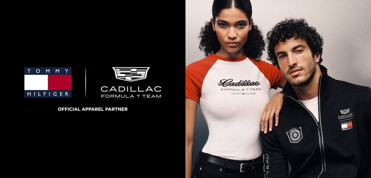Joven mujer con camiseta de Fórmula 1 de Cadillac blanca y roja, y hombre con chaqueta negra con cremallera con los logotipos de Cadillac y Tommy Hilfiger posan juntos.