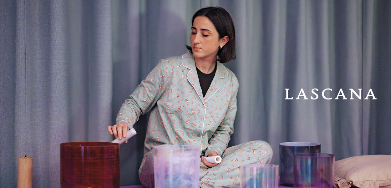 Vrouw in patroonpyjama's zittend met gekruiste benen, die kleurrijke kristallen zangkommen bespeelt met hamers in een rustige binnensituatie.