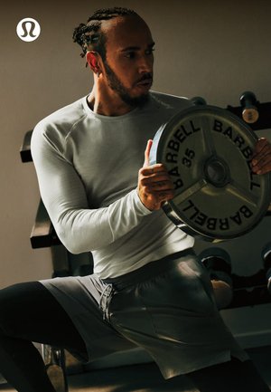 Un athlète en tenue d'entraînement se repose en tenant une plaque de poids de 35 livres dans une salle de sport avec des haltères en arrière-plan.