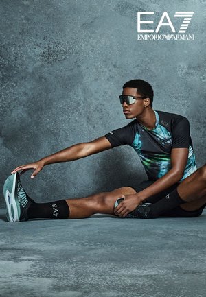 T-shirt de sport à manches courtes, noir, avec un motif abstrait teal et bleu, associé à un short et des chaussettes noirs, mettant en avant des chaussures de sport élégantes.