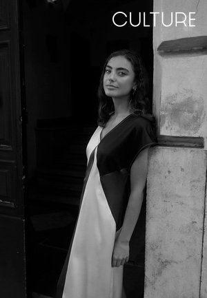 Langes, seidiges Kleid mit schwarzen und weißen Abschnitten und lockerem Sitz. Das Modell steht vor einer strukturierten Wand und zeigt den Fall des Kleidungsstücks.