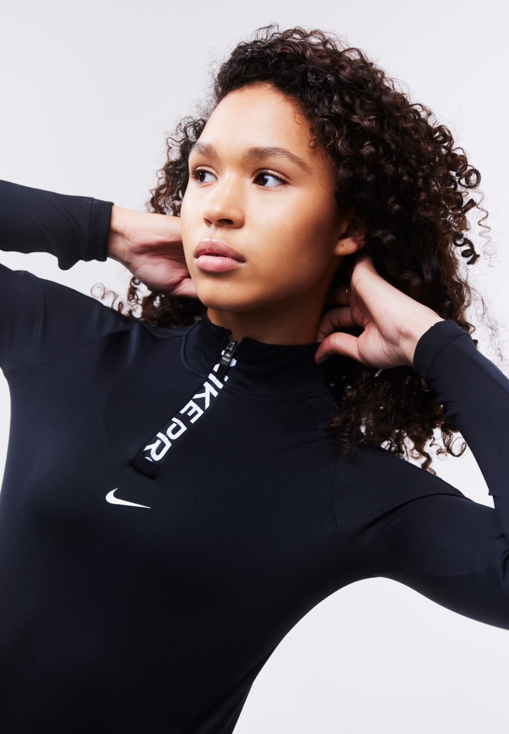 Black athletic long-sleeve top with a quarter-zip, featuring a white Nike logo and bold branding along the zipper. Smooth fabric texture.