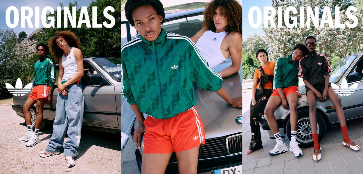 Zwei Personen, die Adidas Originals Kleidung tragen, posieren bei einem silbernen Auto im Freien in einer sonnigen Umgebung mit Bäumen im Hintergrund.
