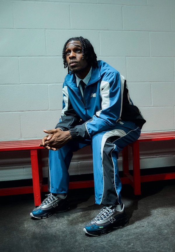 Survêtement bleu, noir et blanc, avec une veste zippée et un pantalon ajusté, associé à des baskets sombres avec des détails en maille et un logo.