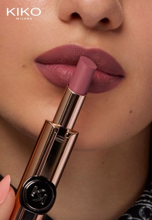 Rouge à lèvres KIKO Milano dans une teinte mauve mat tenu contre des lèvres. Le tube présente une finition rose doré brillant avec un logo noir en accent.