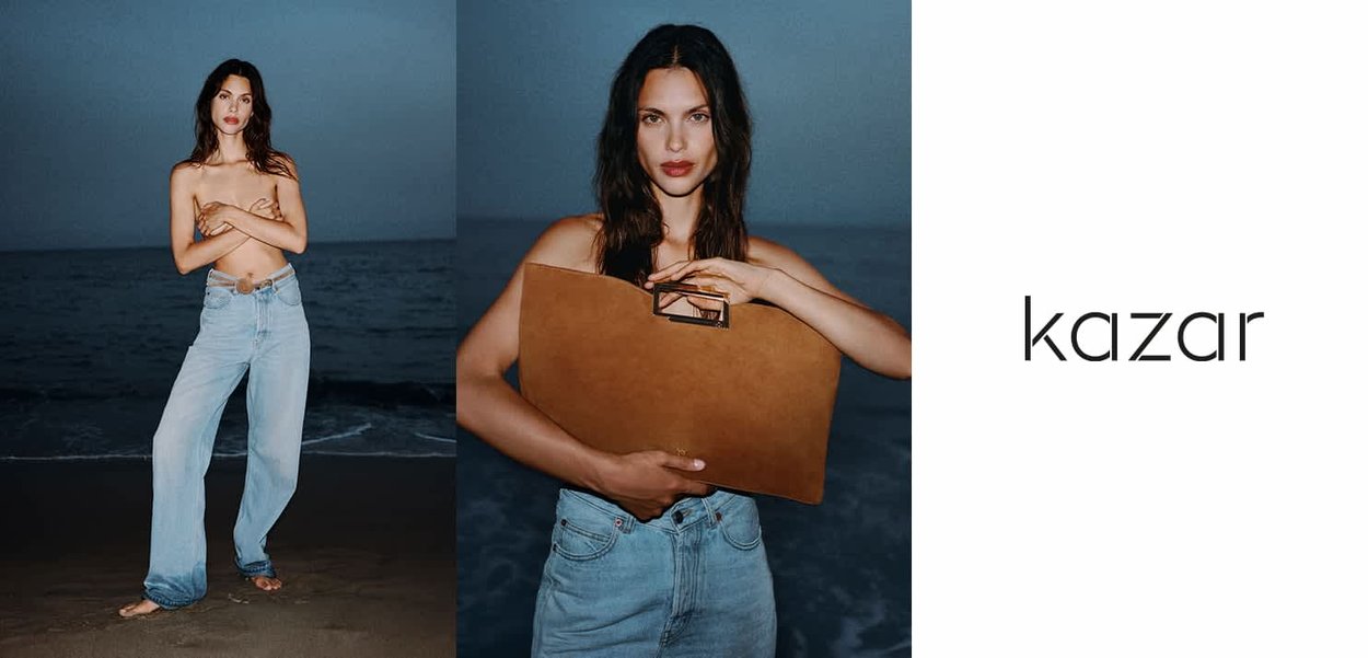 Light blue denim flared jeans and a brown leather folder against a beach background. Dark blue ocean and sky create a serene atmosphere.