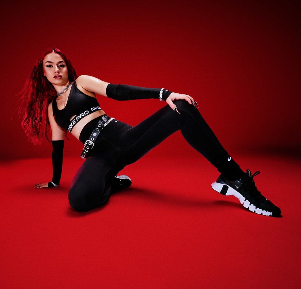 Schwarzes Sport-Crop-Top mit "Nike Pro"-Logo, dazu passende hoch-taillierte Leggings und schwarze Sportschuhe. Der Hintergrund ist einfarbig rot.