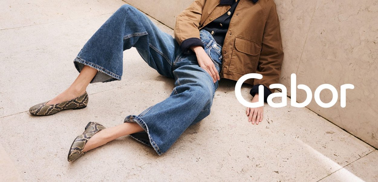Snake-print flats feature a pointed toe design. Paired with wide-leg blue denim jeans and a brown jacket. Clean, simple aesthetic.