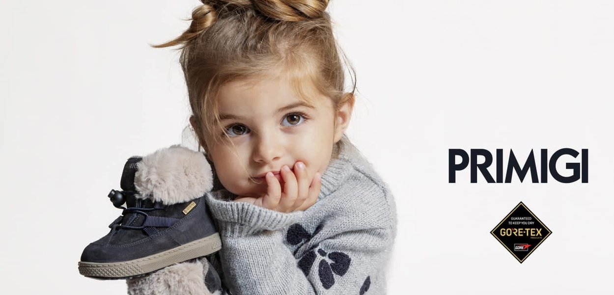 Marineblaue Wildlederschuhe mit einem flauschigen grauen Kragen und schwarzen Schnürsenkeln. Ein Kind hält den Schuh und trägt einen hellgrauen Pullover mit dunkelblauen Akzenten.