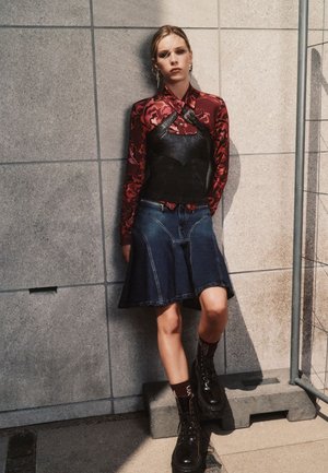 Top corto de cuero negro sobre una camisa de manga larga roja con flores, combinado con una falda de mezclilla azul en línea A y botas de plataforma negras.