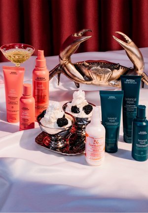 Produits capillaires Aveda dans des tubes et bouteilles roses et verts variés ; plat argenté avec de la crème fouettée et des mûres, à côté d'une sculpture de crabe en bronze.