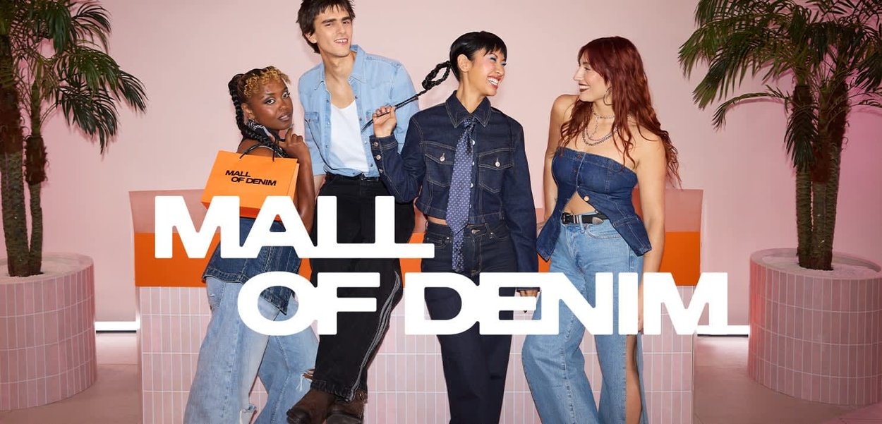 Quattro giovani adulti in denim sorridono e posano con sacchetti della spesa davanti a uno sfondo rosa con piante di palma.