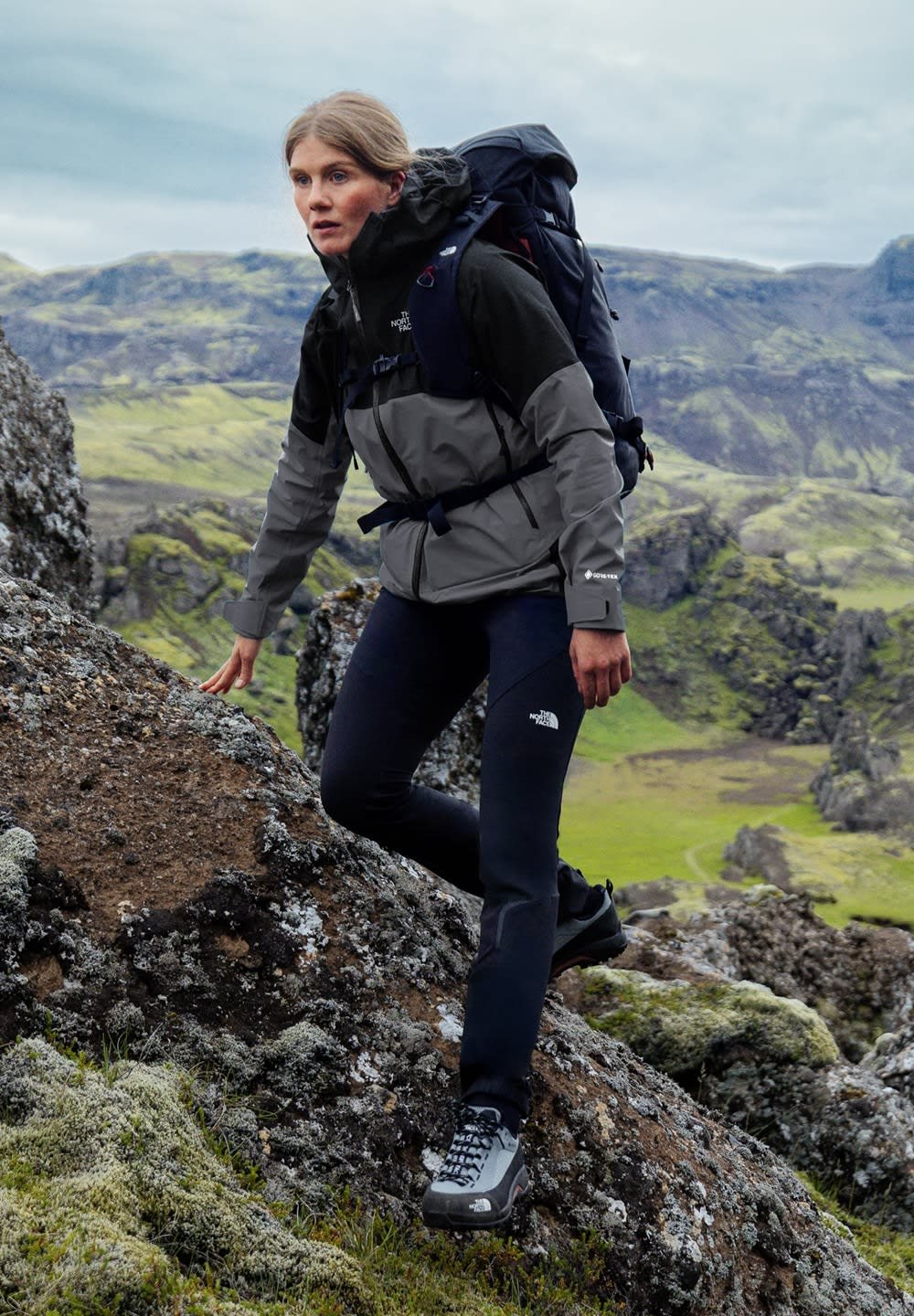 L'attrezzatura da trekking include una giacca grigia e nera, pantaloni neri e solide scarpe grigie. La persona sta scalando un terreno roccioso.