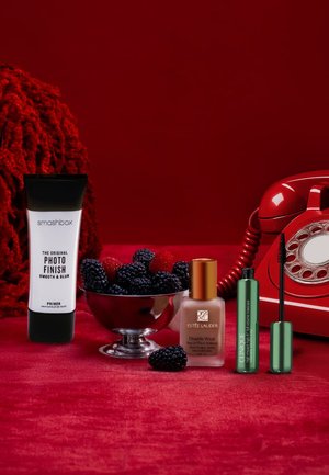 Tubo di primer Smashbox, bottiglia di fondotinta Estee Lauder, mascara Clinique e un telefono vintage rosso su velluto rosso. More in una ciotola d'argento.
