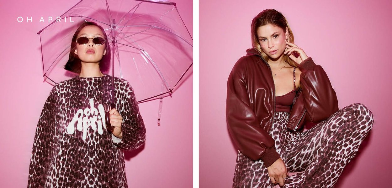 Leopardenmuster-Pullover mit weißem Logo, klarer Regenschirm und brauner Bomberjacke; zweites Modell in maroonem Oberteil mit passenden Hosen. Rosa Hintergrund.