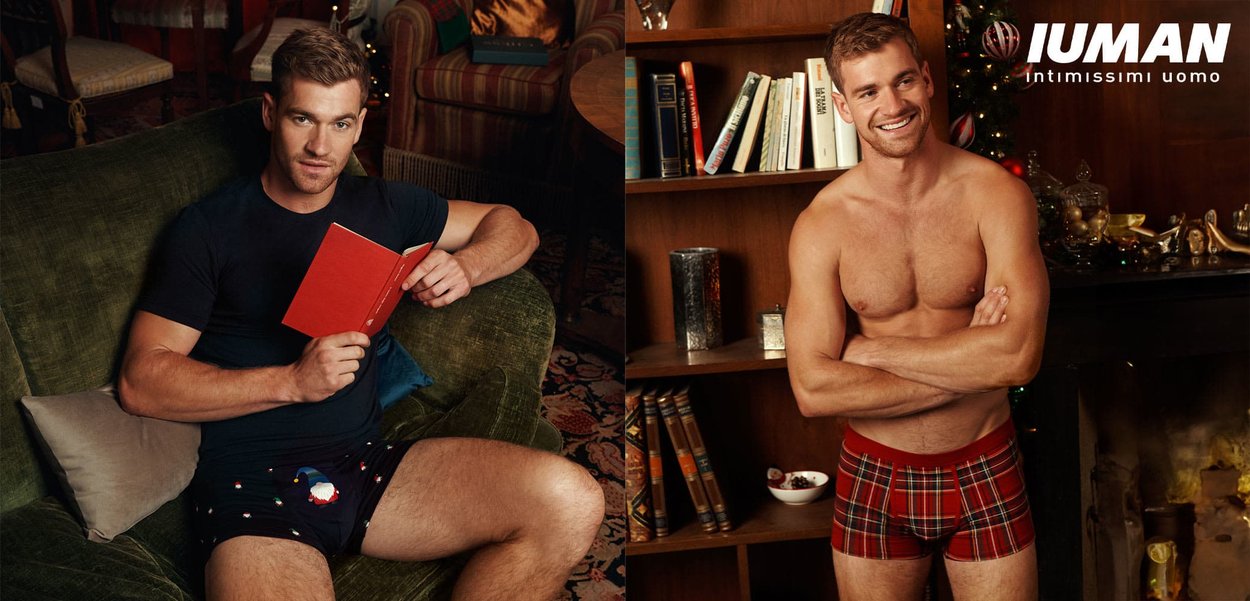 Rote karierte Boxershorts mit eng anliegender Passform, versehen mit einem einfarbigen Bund und einem karierten Muster. Das Modell ist oben ohne und lächelt.