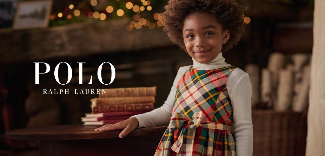 Ung jente i rutet kjole med sløyfe smiler, lener seg på et bord med stabler av gamle bøker og varme, blinkende lys i bakgrunnen.