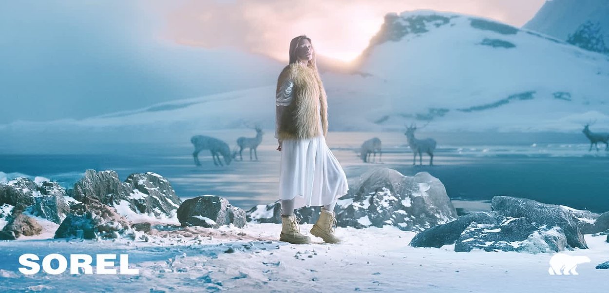 SOREL Winterstiefel in Beige, mit einem robusten Design und strukturiertem Material, getragen mit einem weißen Kleid vor einer schneebedeckten Landschaft.