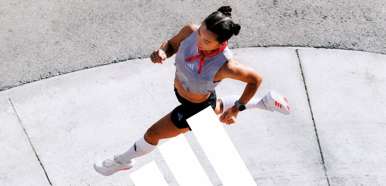 Mujer con ropa deportiva corriendo sobre una superficie pavimentada curva con el logo de Adidas, lleva una bufanda roja y un reloj deportivo.