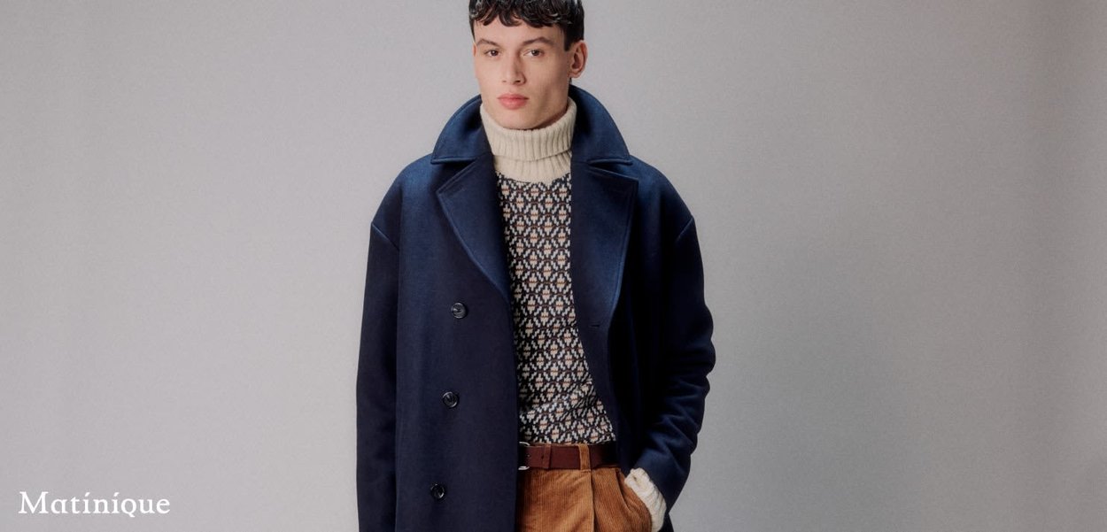 Marineblauer Wollmantel mit großen Revers und Knöpfen über einem gemusterten creme- und marineblauen Pullover, kombiniert mit braunen Cordhosen. Weiche Textur.