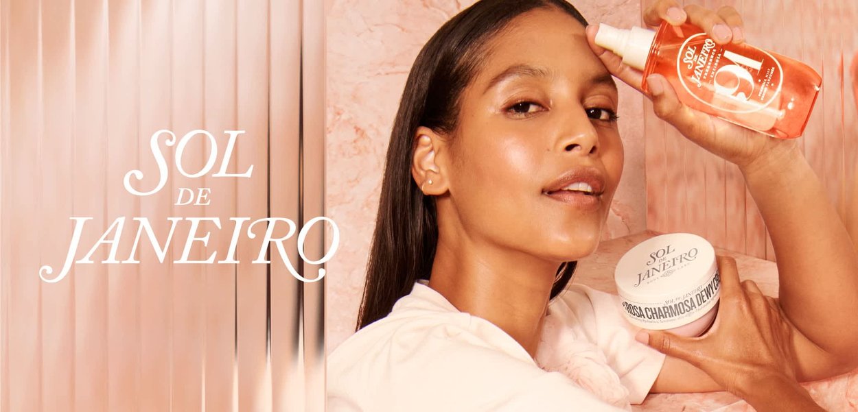 Vrouw met gladde huid houdt Sol de Janeiro spray dicht bij het voorhoofd en een crèmecontainer tegen een perzikmarmeren en roze achtergrond.