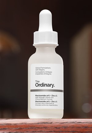 Petit flacon compte-gouttes en verre dépoli portant l'étiquette The Ordinary Niacinamide 10% + Zinc 1% sérum, posé sur une surface en bois.