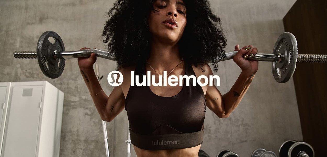 Mujer levantando pesas con barra sobre los hombros en el gimnasio, vistiendo un sujetador deportivo negro de lululemon con cabello rizado.