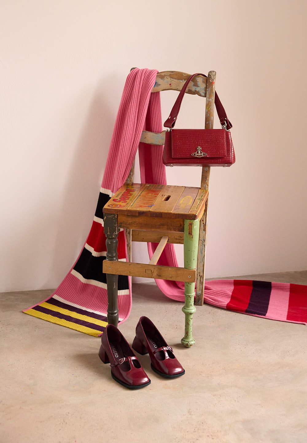 Κόκκινη δερμάτινη τσάντα με υφή και ασημί αξεσουάρ, σε συνδυασμό με μπορντώ ψηλοτάκουνα παπούτσια με κοπή μπροστά, πάνω σε ξύλινη καρέκλα.