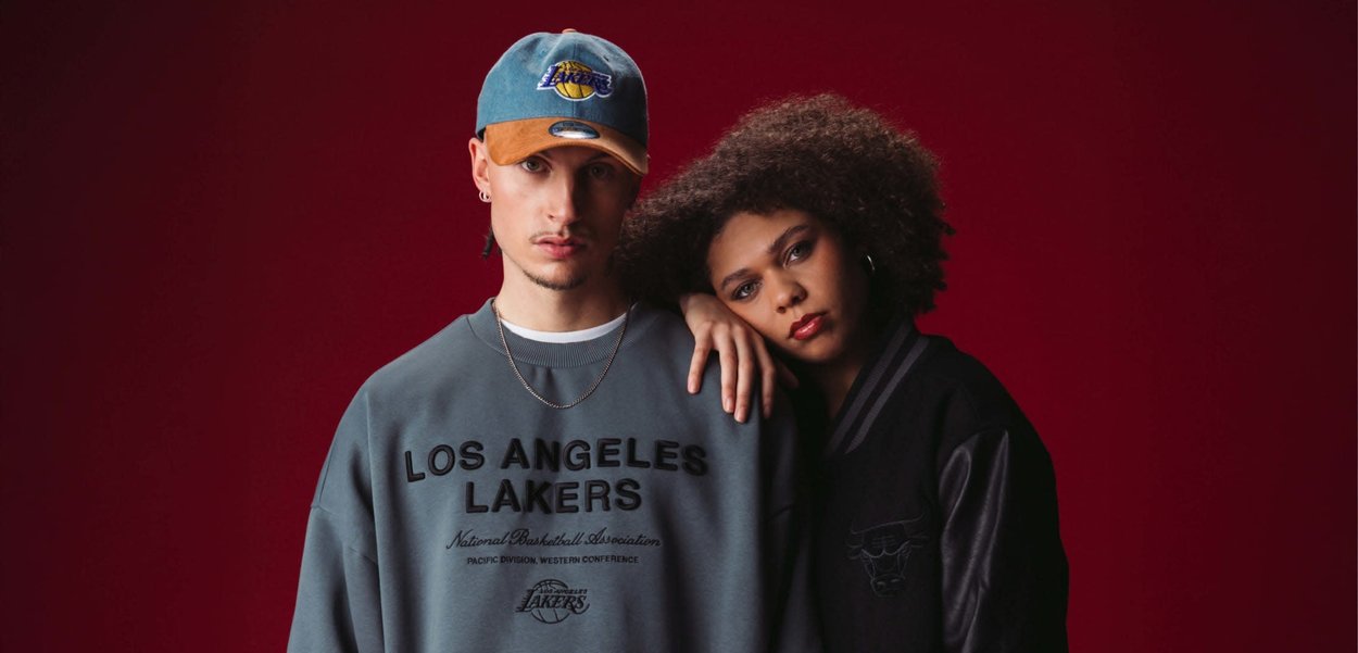 Grauer Sweatshirt mit dem Text "LOS ANGELES LAKERS", kombiniert mit einer schwarzen Jacke, die Lederärmel hat und ein Logo des Basketballteams auf der Vorderseite trägt.